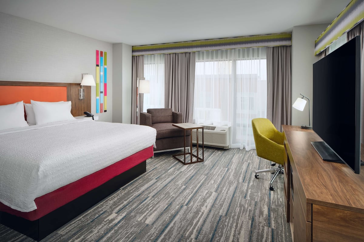 A hotel room with a large bed, a desk with a TV, a chair, and a small table.