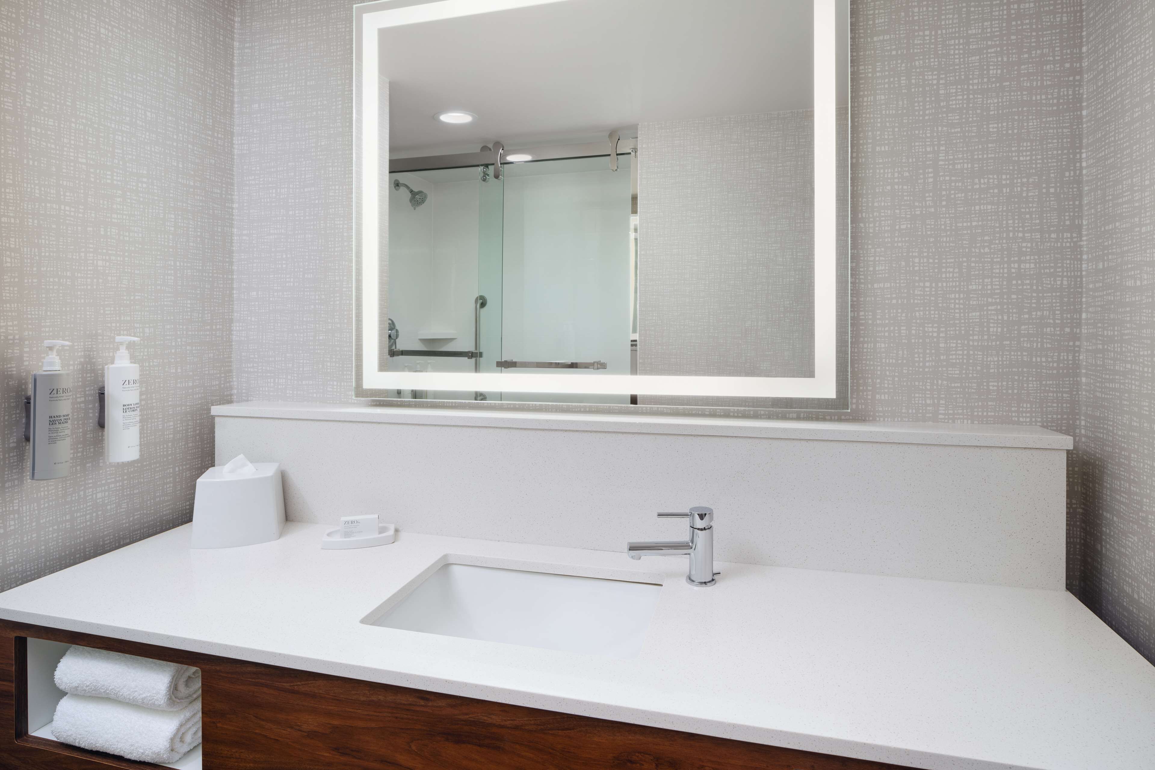 Un baño moderno con un espejo grande, un lavamanos blanco y una cabina de ducha de vidrio.