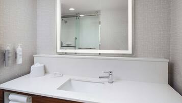 Un baño moderno con un espejo grande, un lavamanos blanco y una cabina de ducha de vidrio.