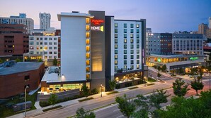A Hampton Inn hotel with a modern design, featuring a prominent 'HOME 2' sign, surrounded by other buildings and a well-lit street. - Hampton Inn Towson Downtown (Towson)