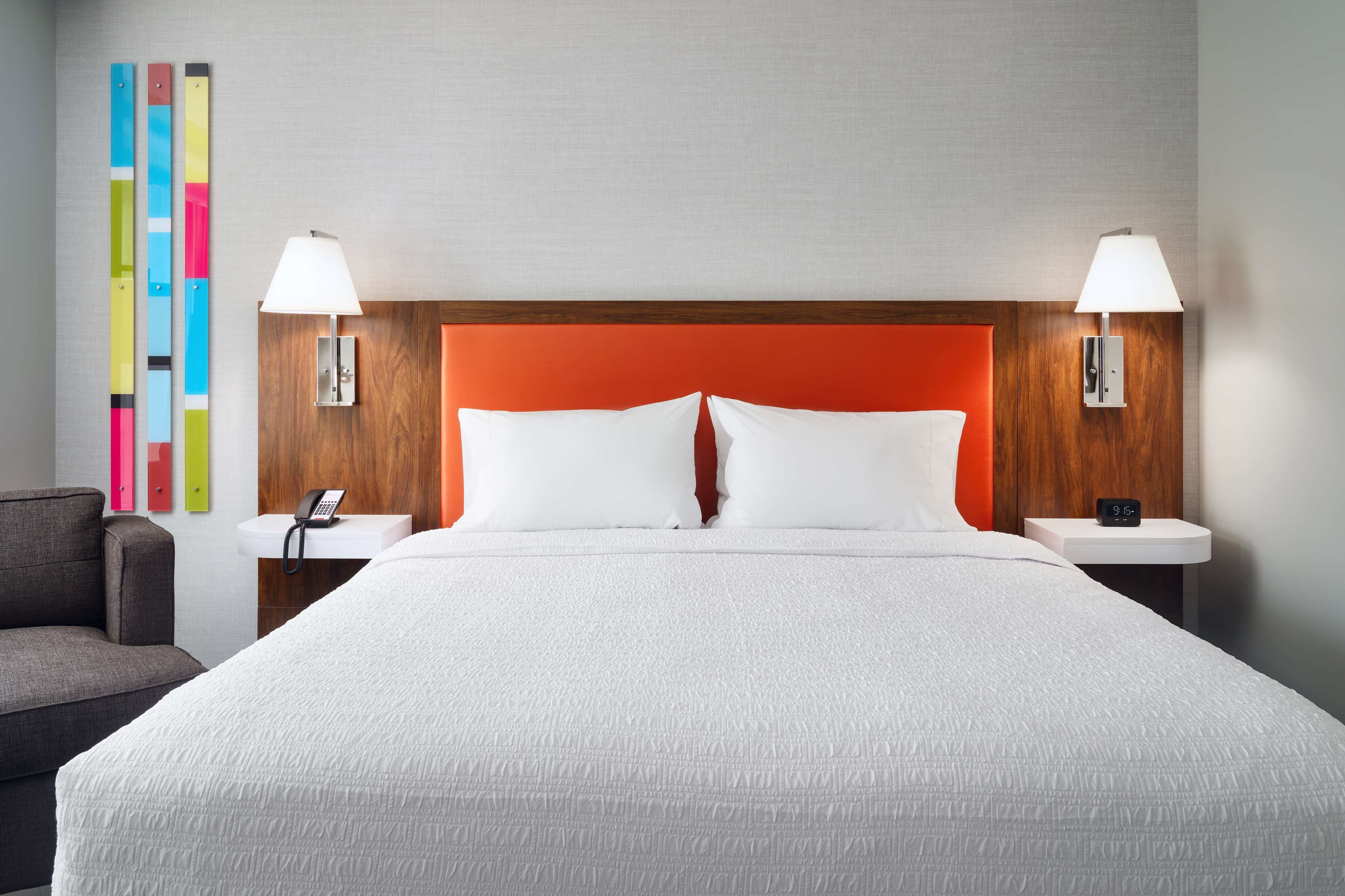 Una habitación de hotel con una cama grande, dos mesitas de noche, un teléfono y una lámpara de pared.