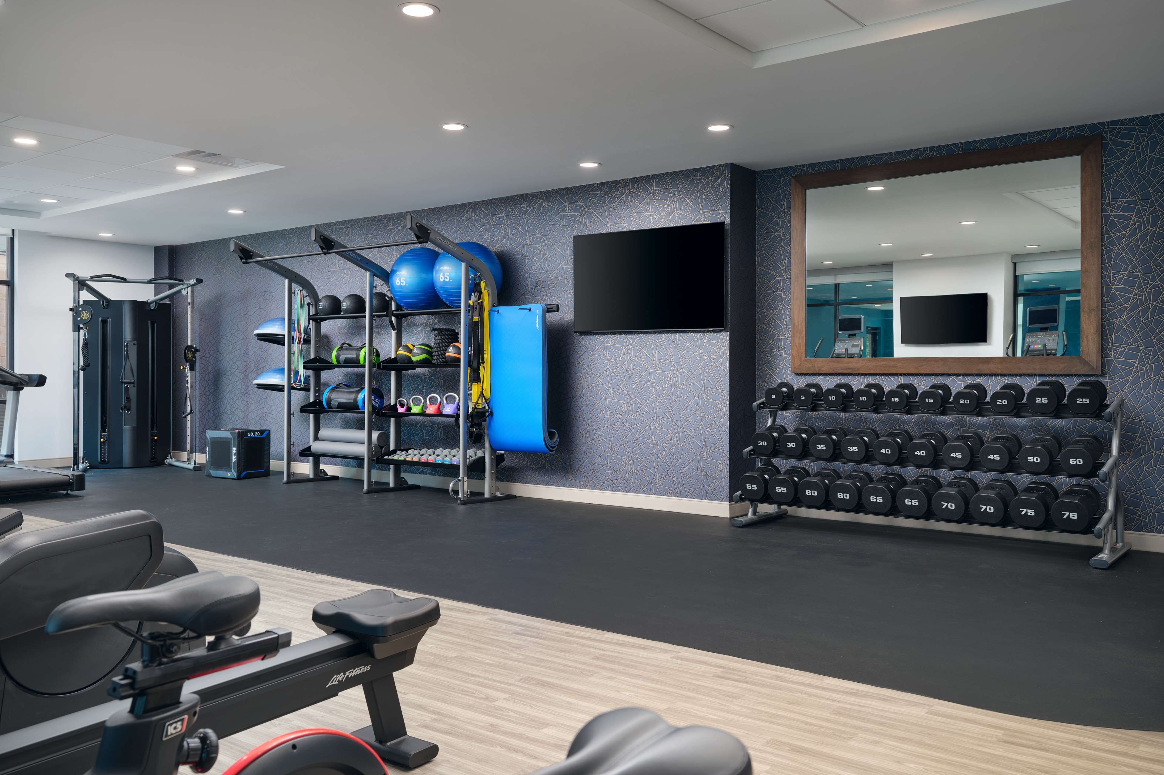 Ein Fitnessraum mit Trainingsgeräten, Laufband und Spiegel.