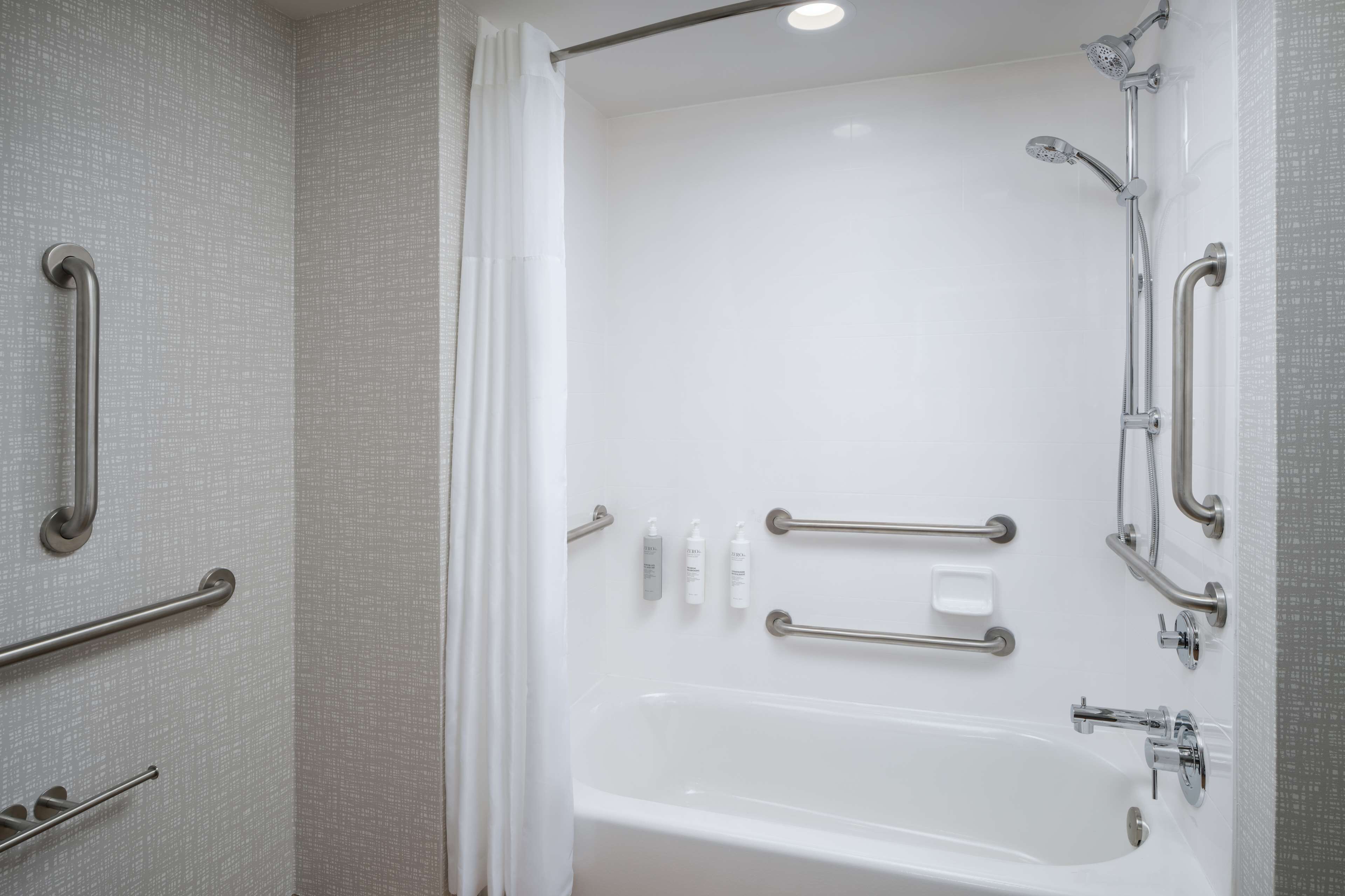 A modern bathroom with a bathtub, grab bars, and a showerhead.