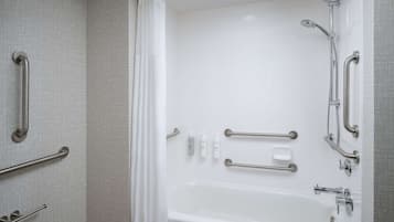 A modern bathroom with a bathtub, grab bars, and a showerhead.