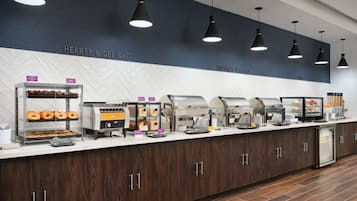 Disposição de buffet com diversos pontos de comida, incluindo uma mesa com donuts e uma máquina de café.