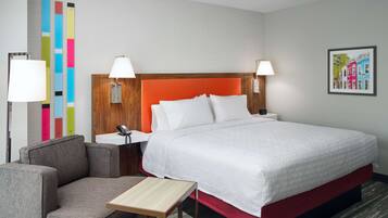 A hotel room with a large bed, two bedside lamps, a small table, a sofa, and a colorful wall decoration.