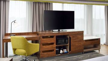 A modern hotel room with a wooden desk, a flat-screen TV, a yellow chair, a microwave, and a coffee maker.
