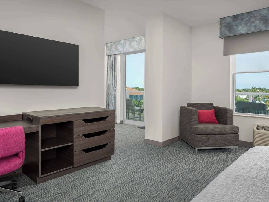 Een moderne hotelkamer met een grote flatscreen-tv, een bureau met lades, een comfortabele fauteuil en een groot raam met uitzicht op de omgeving.