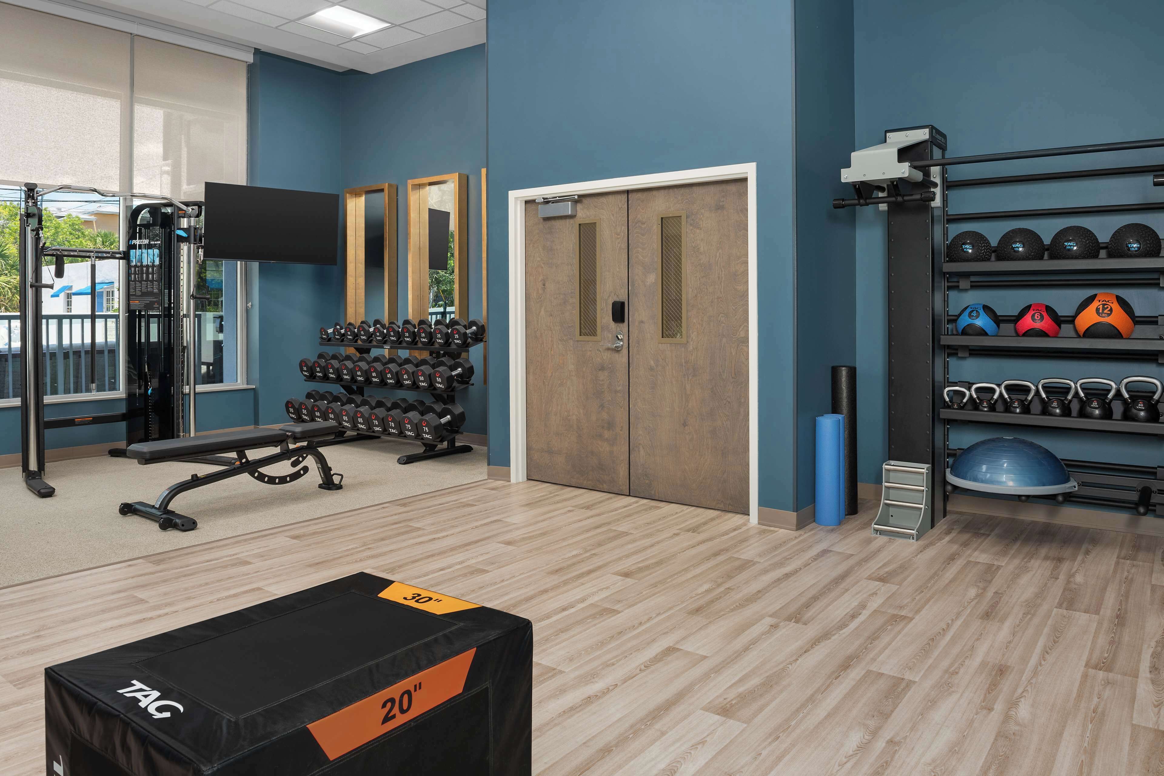 Et træningscenter med vægtaflastningsudstyr, en bænk og et vægmonteret stativ med kettlebells.