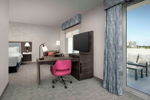 Une chambre d’hôtel moderne équipée d’un lit, d’un bureau, d’une chaise, d’une télévision et d’un balcon avec des sièges.