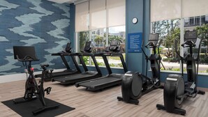 Une salle de sport équipée de tapis de course, d’un vélo elliptique et d’un vélo d’appartement, avec de grandes fenêtres et un mur décoré de motifs.