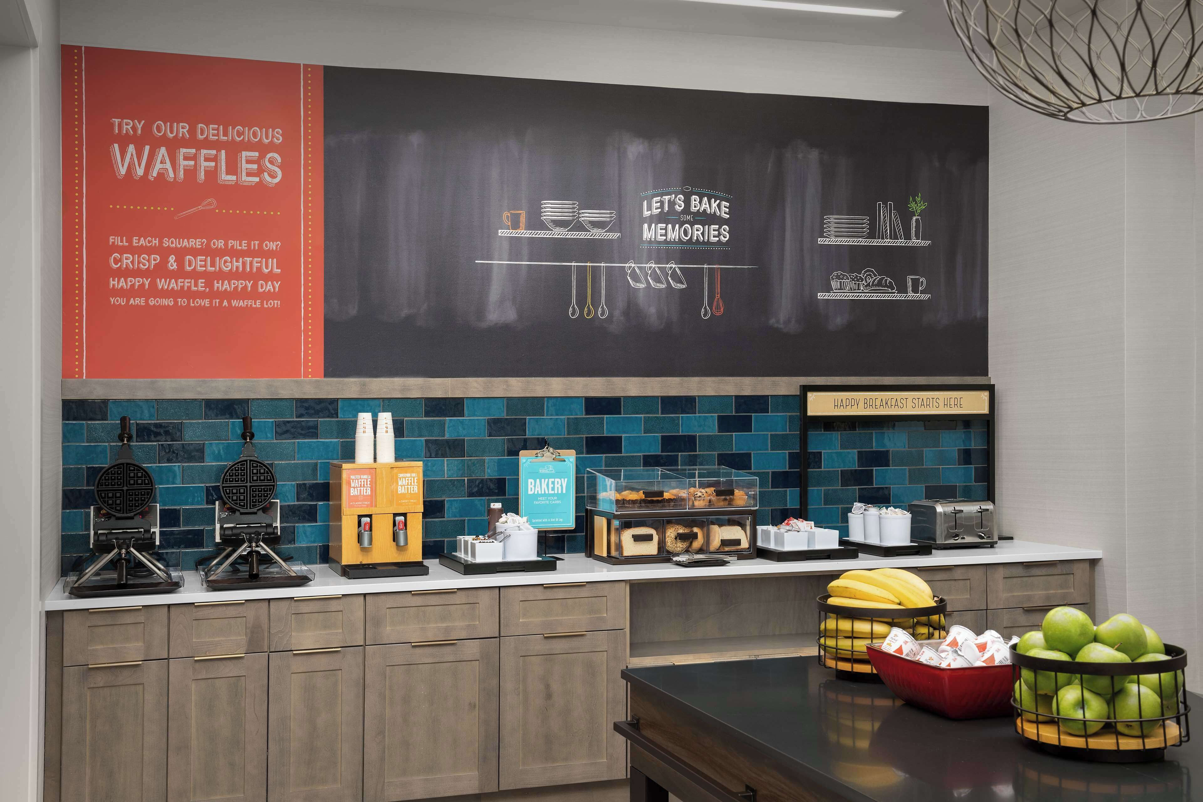 A kitchen area with waffle makers, a bakery sign, and breakfast items on the counter.