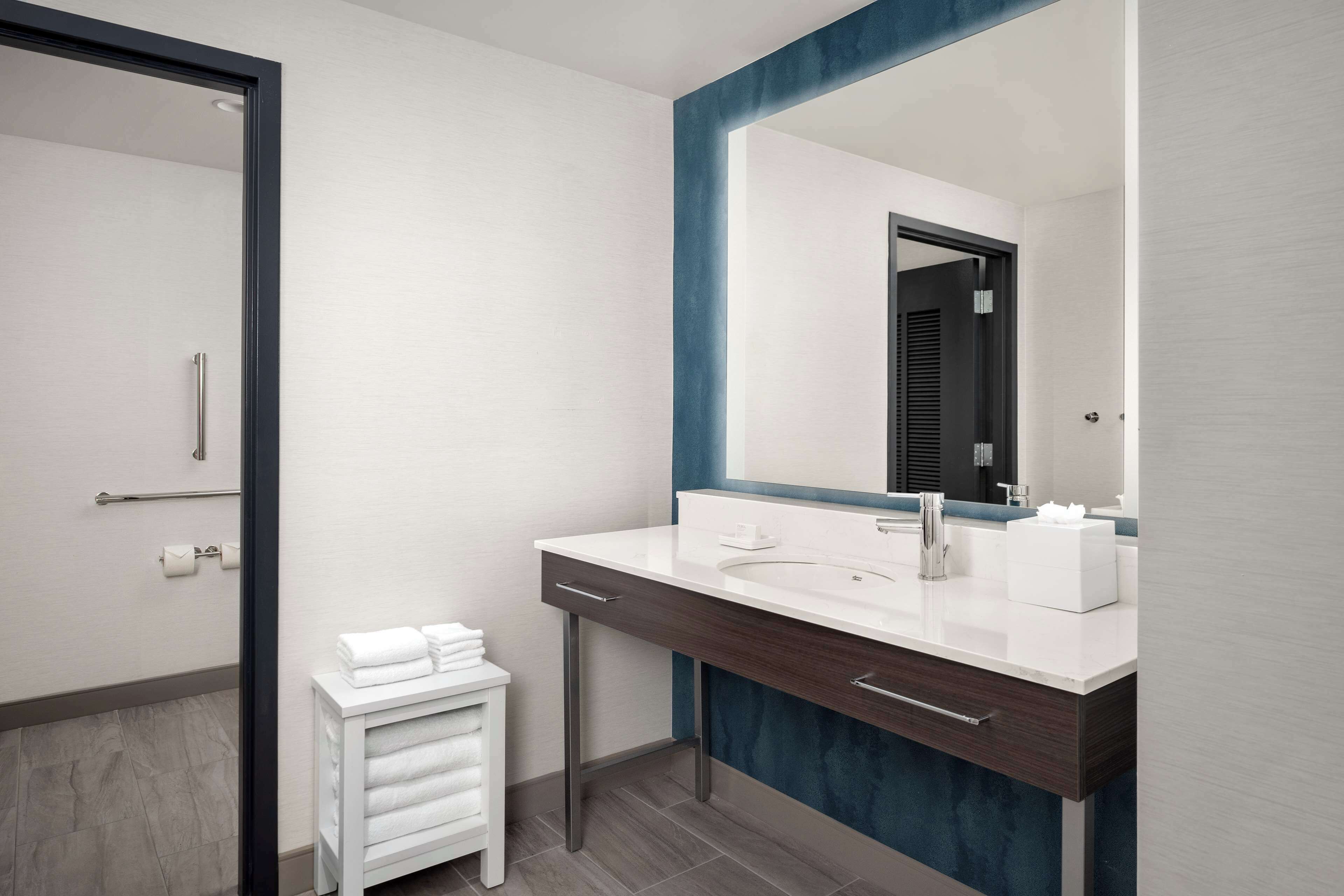 A modern bathroom with a white vanity, a large mirror, and a towel rack.
