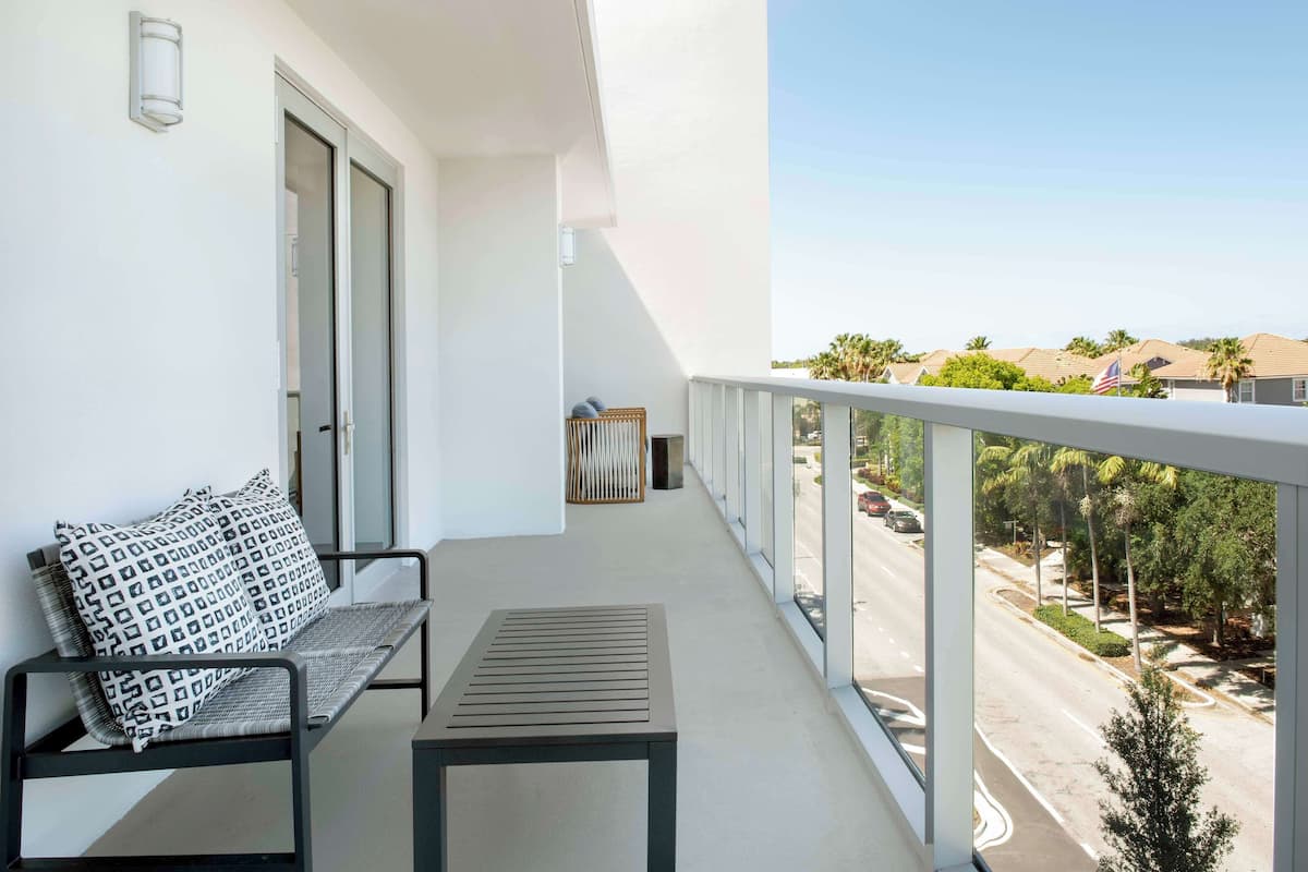A balcony with a seating area, a view of a street, and a clear sky.