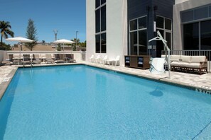 A swimming pool with lounge chairs and umbrellas, a sofa, and a changing station.