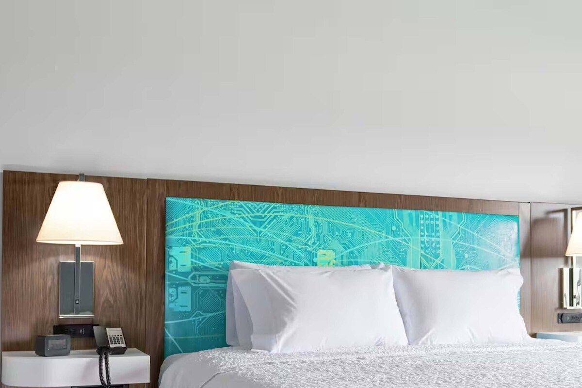 Ein Hotelzimmer mit Bett, Nachttisch mit Lampe, Telefon und Wand mit Schaltungsdesign.
