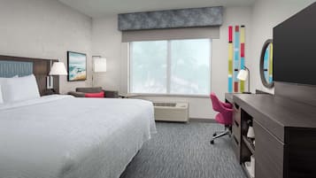 A hotel room with a large bed, a desk, a chair, a window with a view, and a wall with colorful decor.