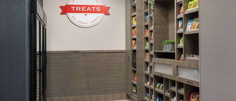 Un rayon dédié aux collations et aux produits divers, avec une enseigne indiquant « Friandises », des étagères bien organisées et un sol carrelé.