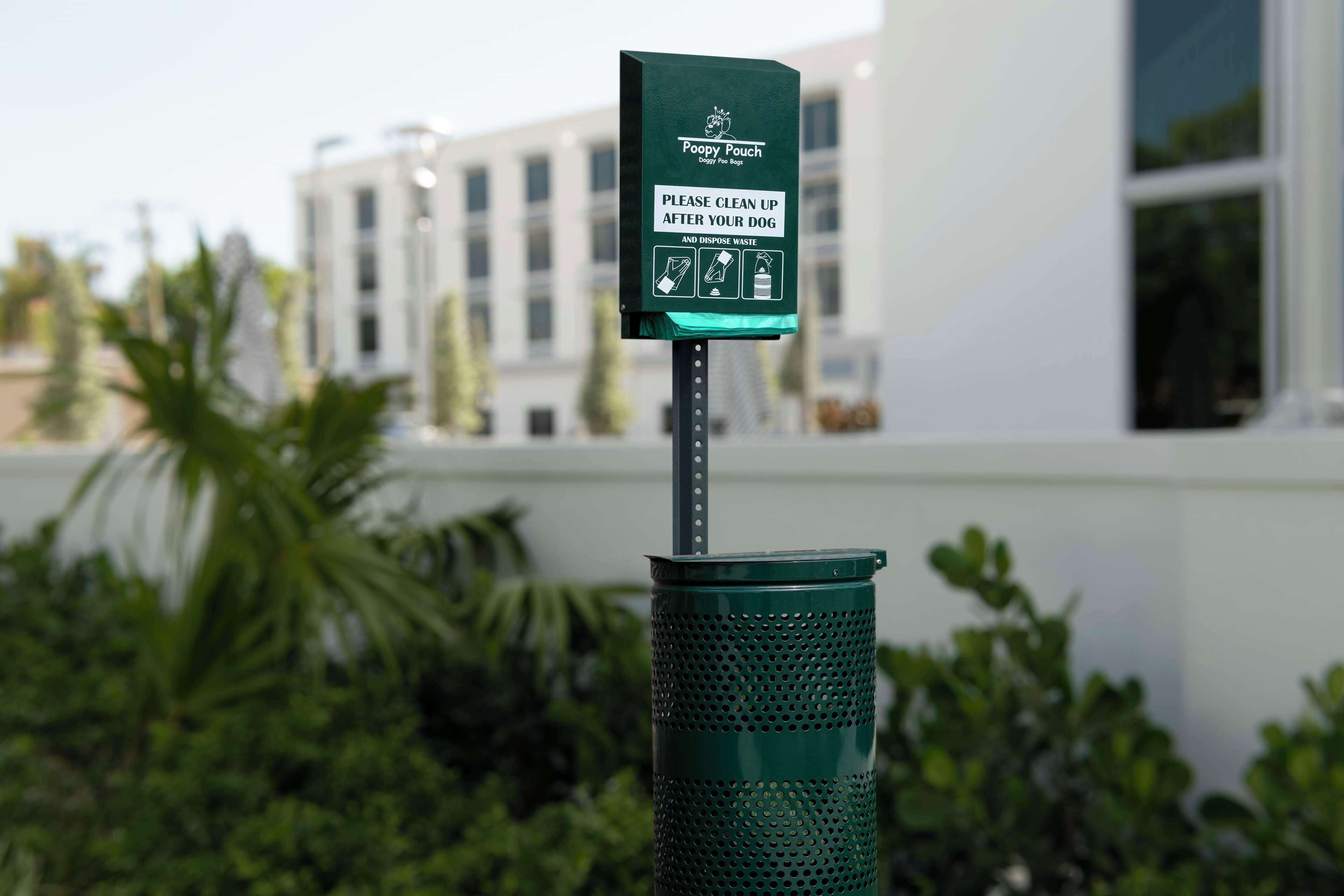 A green trash bin with a sign instructing to clean up after pets and dispose of waste.