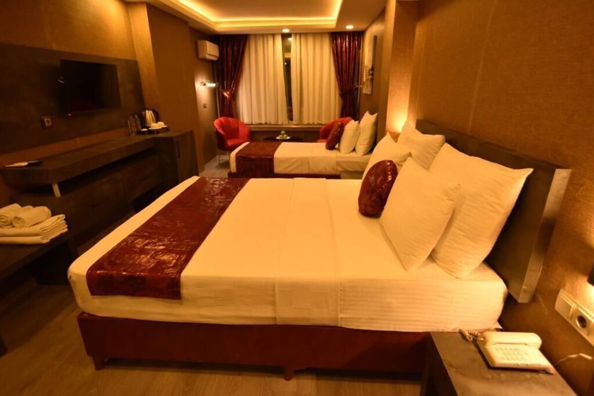 A hotel room with a large bed, a TV, a desk with a phone, and a window with curtains.