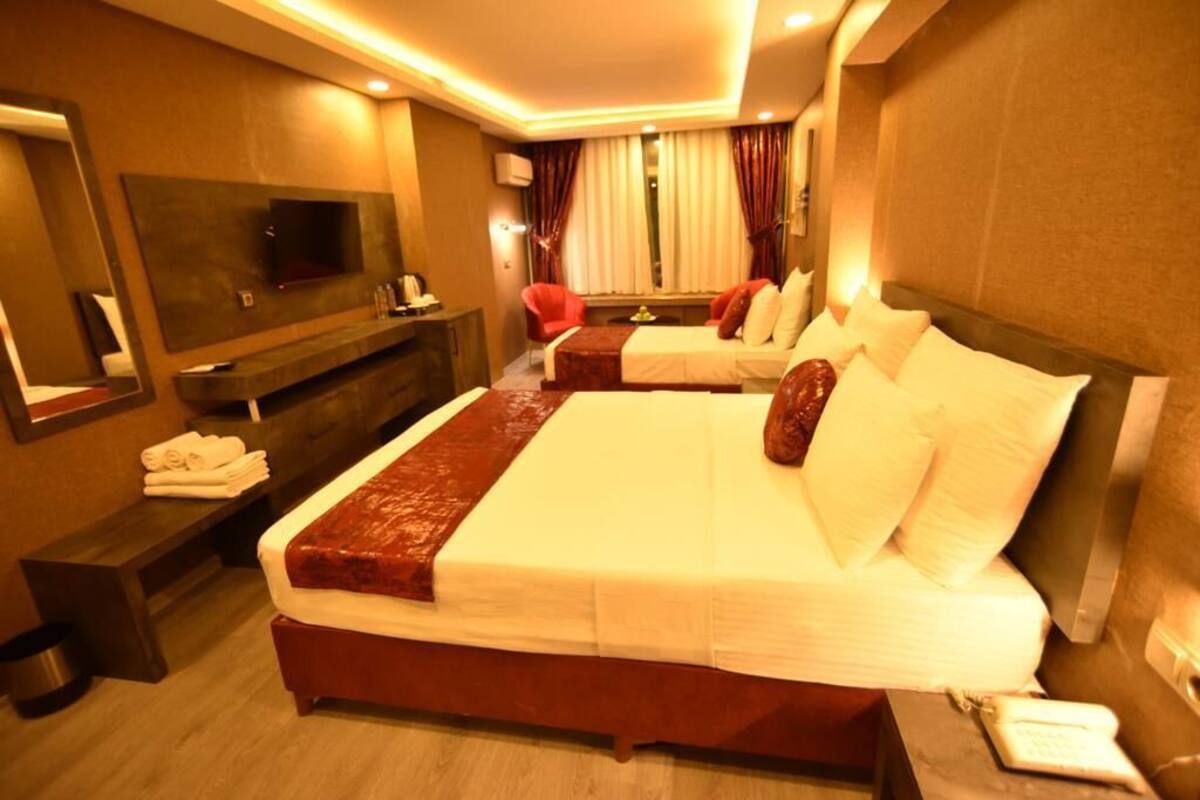 A hotel room with a large bed, a TV mounted on the wall, a bedside table with a phone, and a bench with towels.