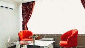 A room with a glass-top table, two red chairs, a small white stool, a vase with flowers, and a window with curtains. - Swiss Inn Hotel Mersin (Mersin)