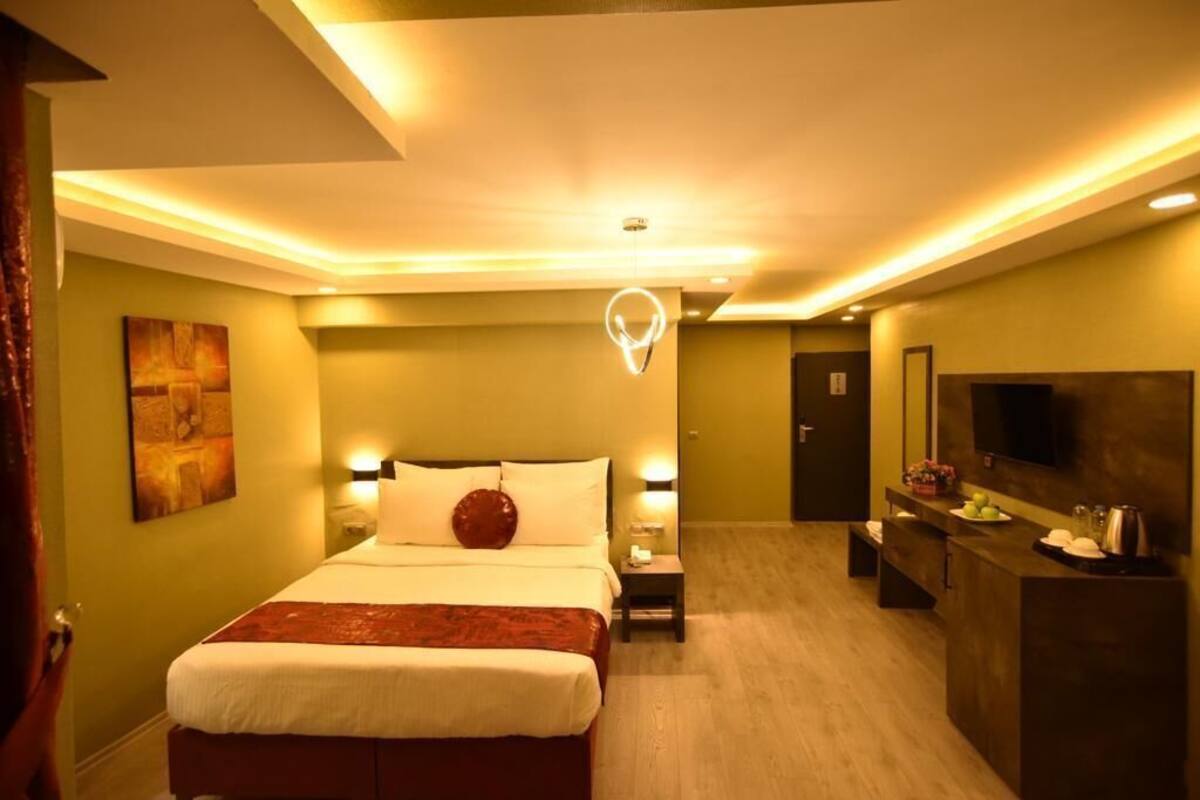 A hotel room with a bed, bedside tables, a desk, a mirror, and a television.