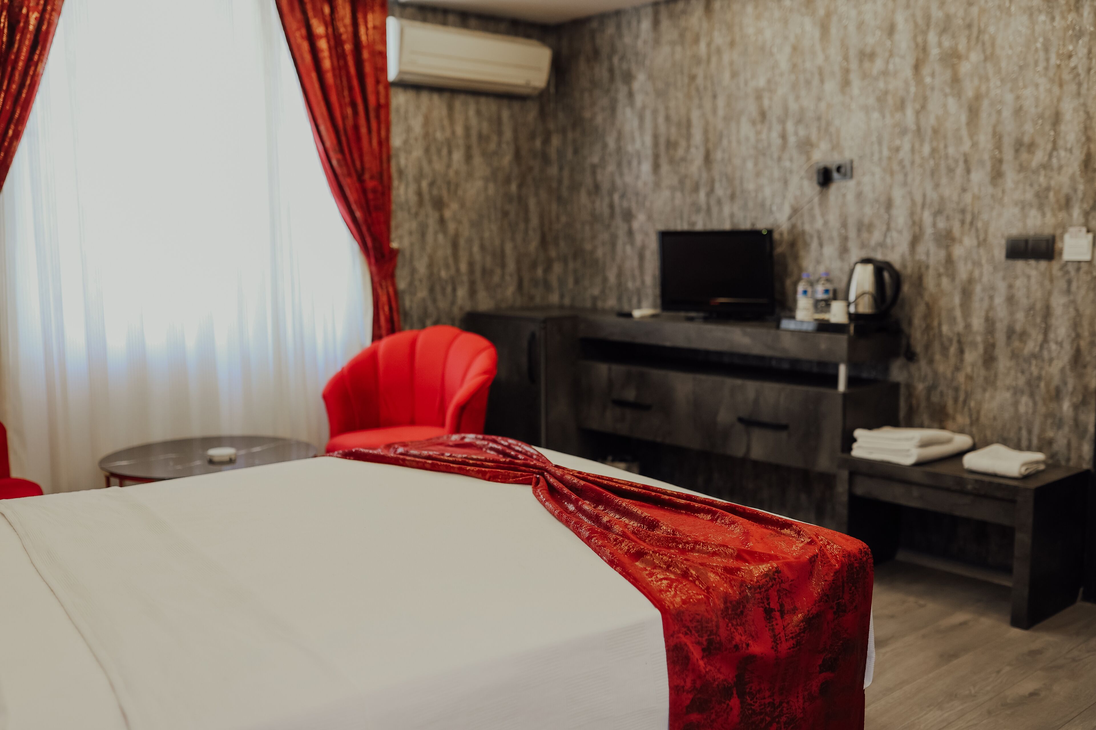 Habitación de hotel con cama, una silla roja, un escritorio con computadora y televisión.