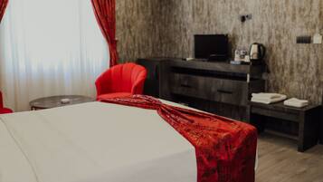 Habitación de hotel con cama, una silla roja, un escritorio con computadora y televisión.
