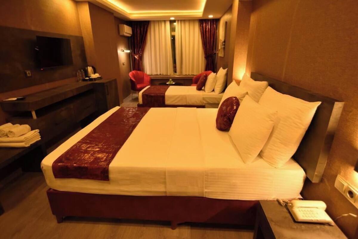 A hotel room with a large bed, a TV, a desk with a phone, and a window with curtains.