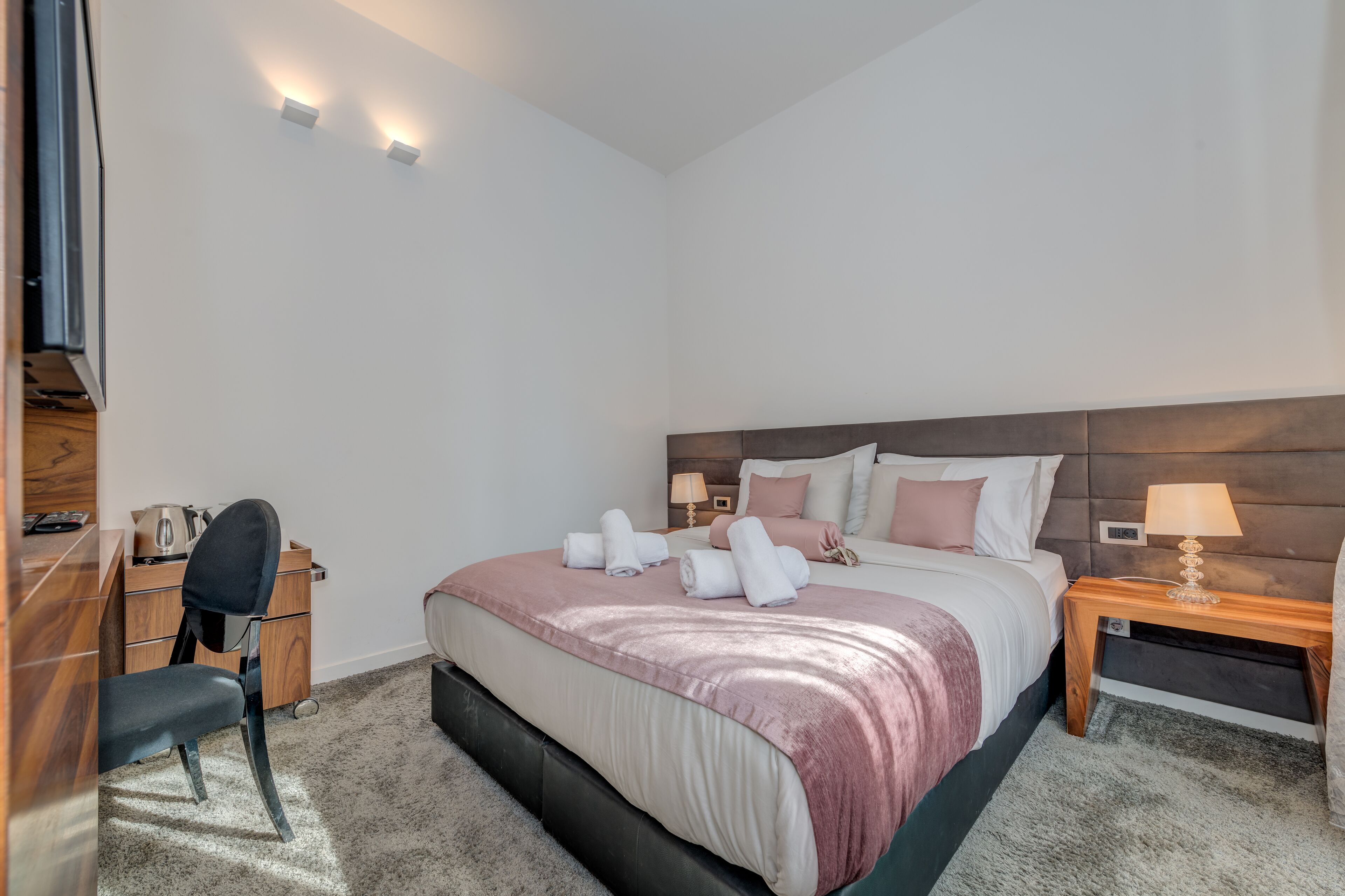 A hotel room with a bed, bedside tables, a desk, and a chair.