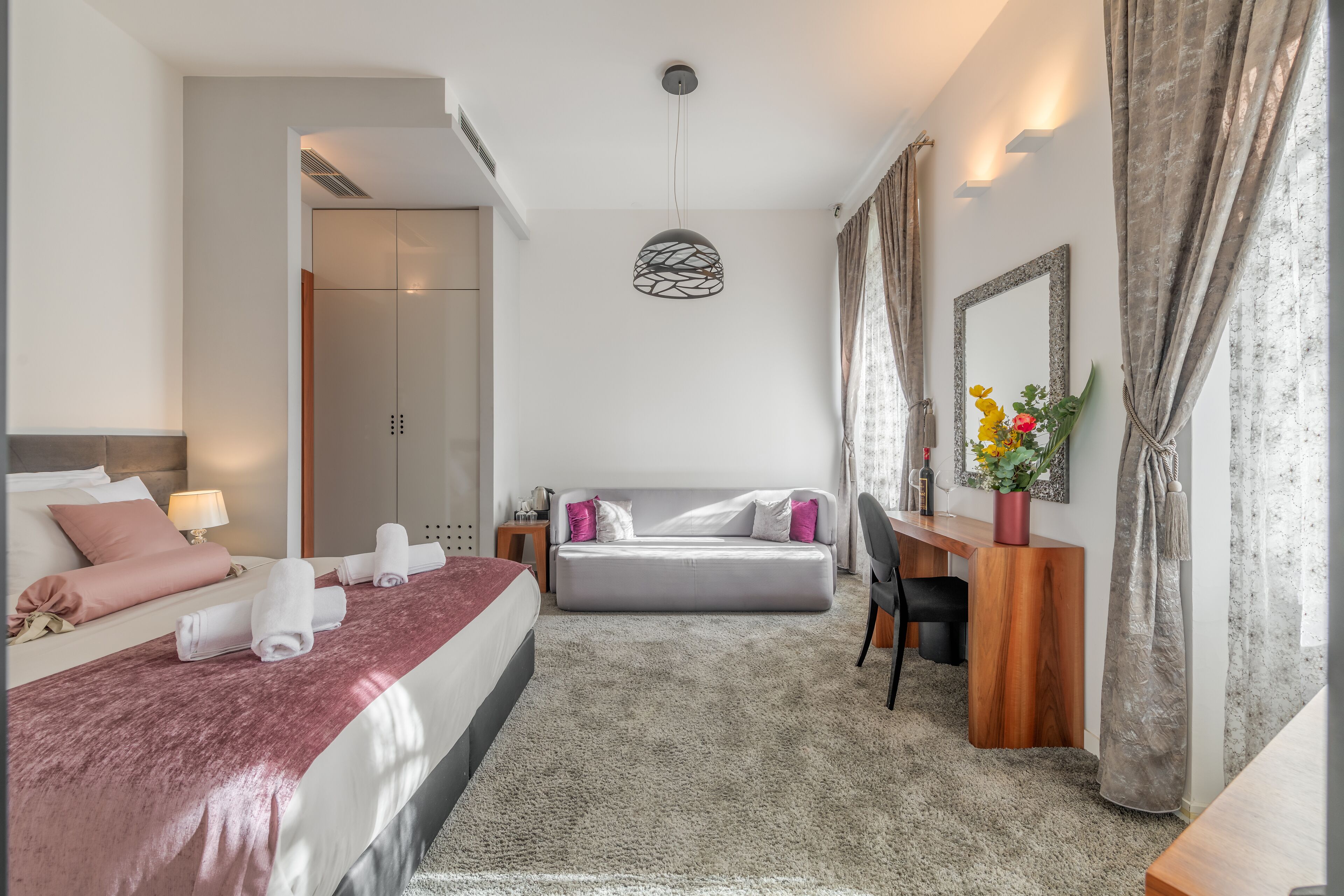 Une chambre d’hôtel moderne équipée d’un lit, d’un bureau, d’une chaise, d’un miroir et d’un vase avec des fleurs.