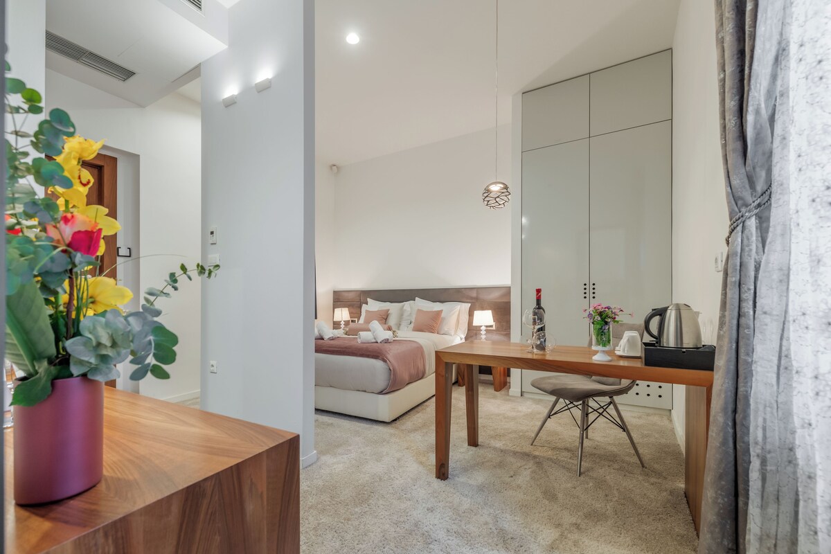A modern hotel room with a bed, bedside table, and a dining area.