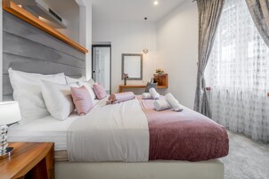 Um quarto moderno com uma cama grande, uma mesa de cabeceira, um criado-mudo, um espelho e uma janela com cortinas.