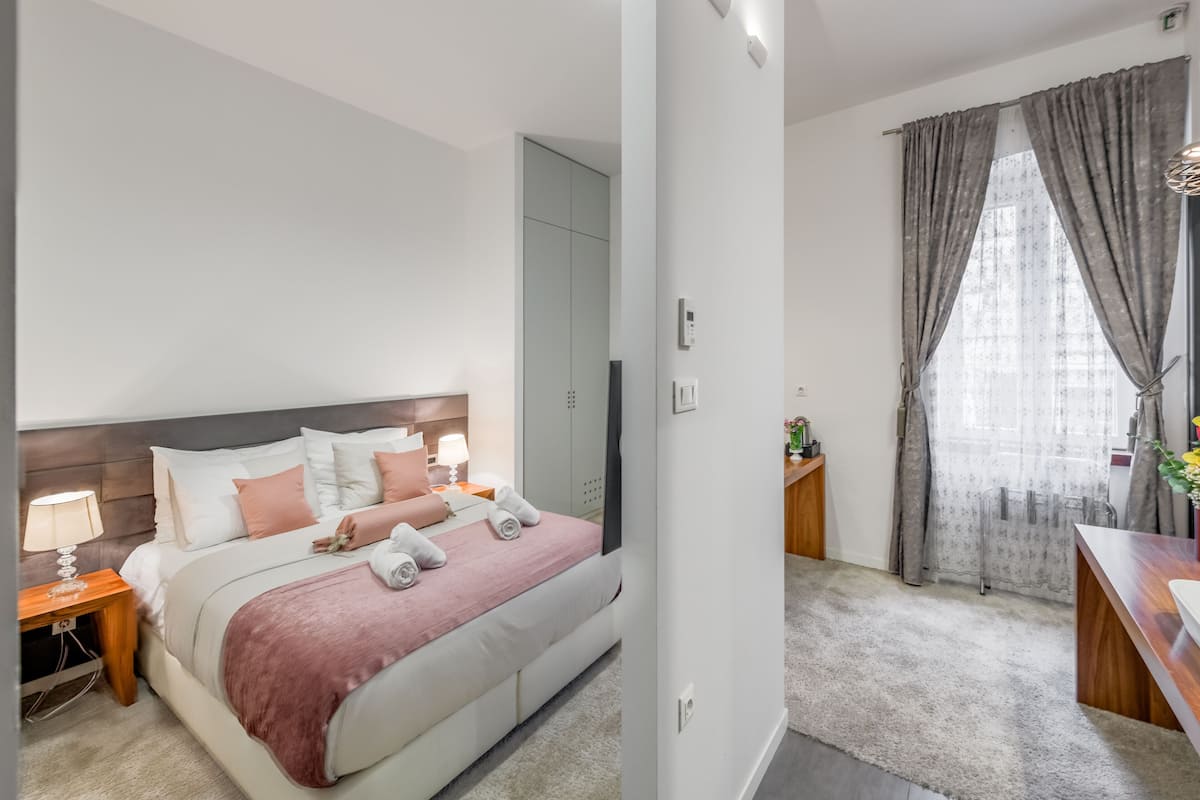 Un dormitorio moderno con una cama grande, mesitas de noche, un armario y vistas a una ventana con cortinas.