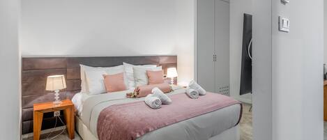 A modern bedroom with a large bed, bedside tables, a headboard, and a shower area.