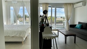 Habitación de hotel con cama, escritorio con lámpara, sofá y vista a la playa.