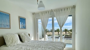 Un dormitorio con cama, ventana con cortinas y vista al mar.