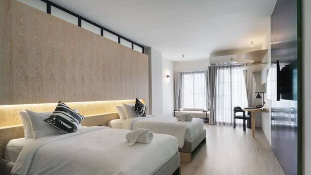 Quarto de hotel moderno com duas camas, uma escrivaninha e um espaço de estar.