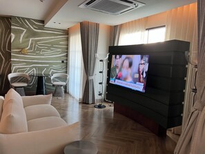 A modern living room with a flat-screen TV, a sofa, and a coffee table. - Hotel Sapin (Bangkok)