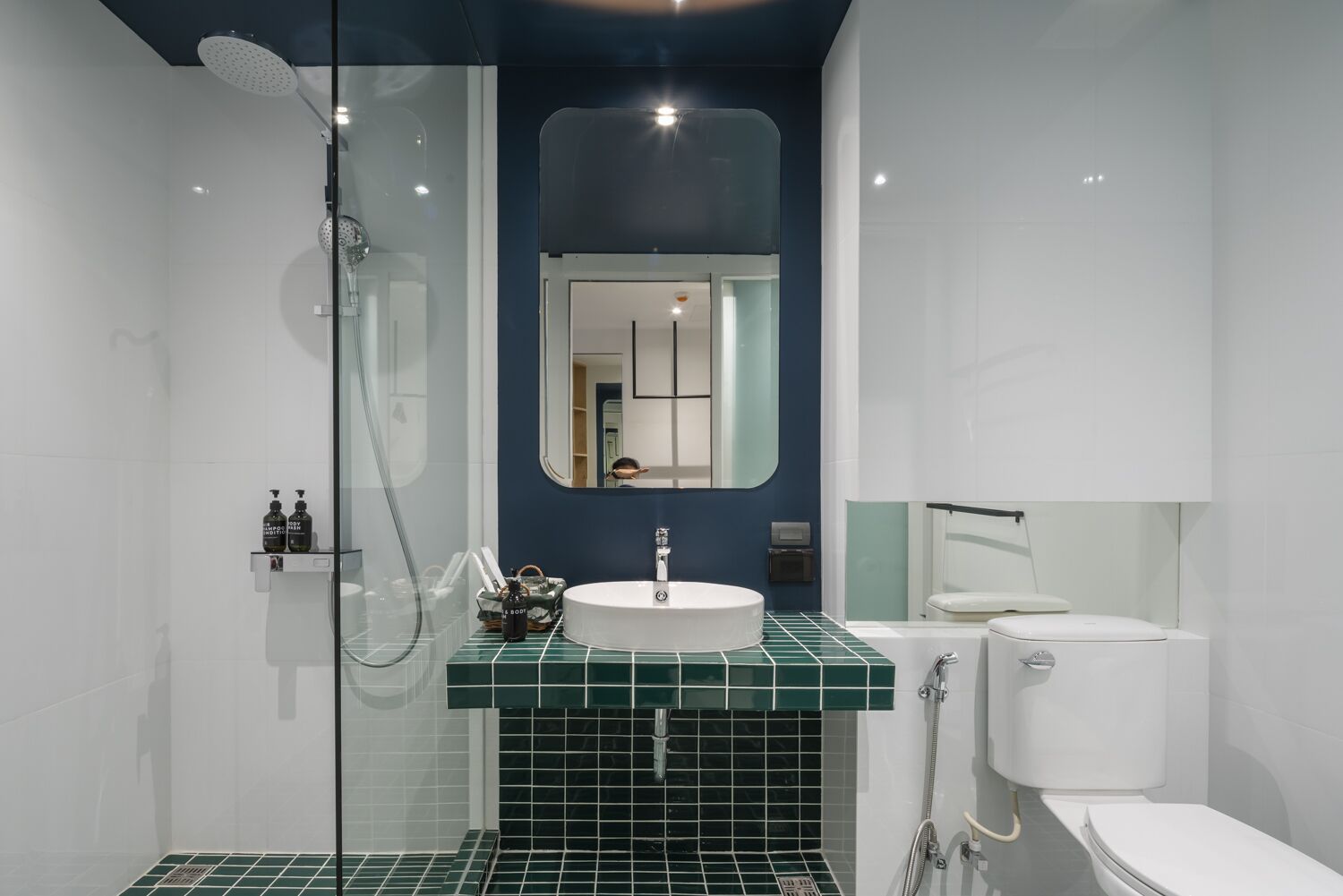 A modern bathroom with a glass-enclosed shower, a white toilet, and a sink with a green-tiled countertop.