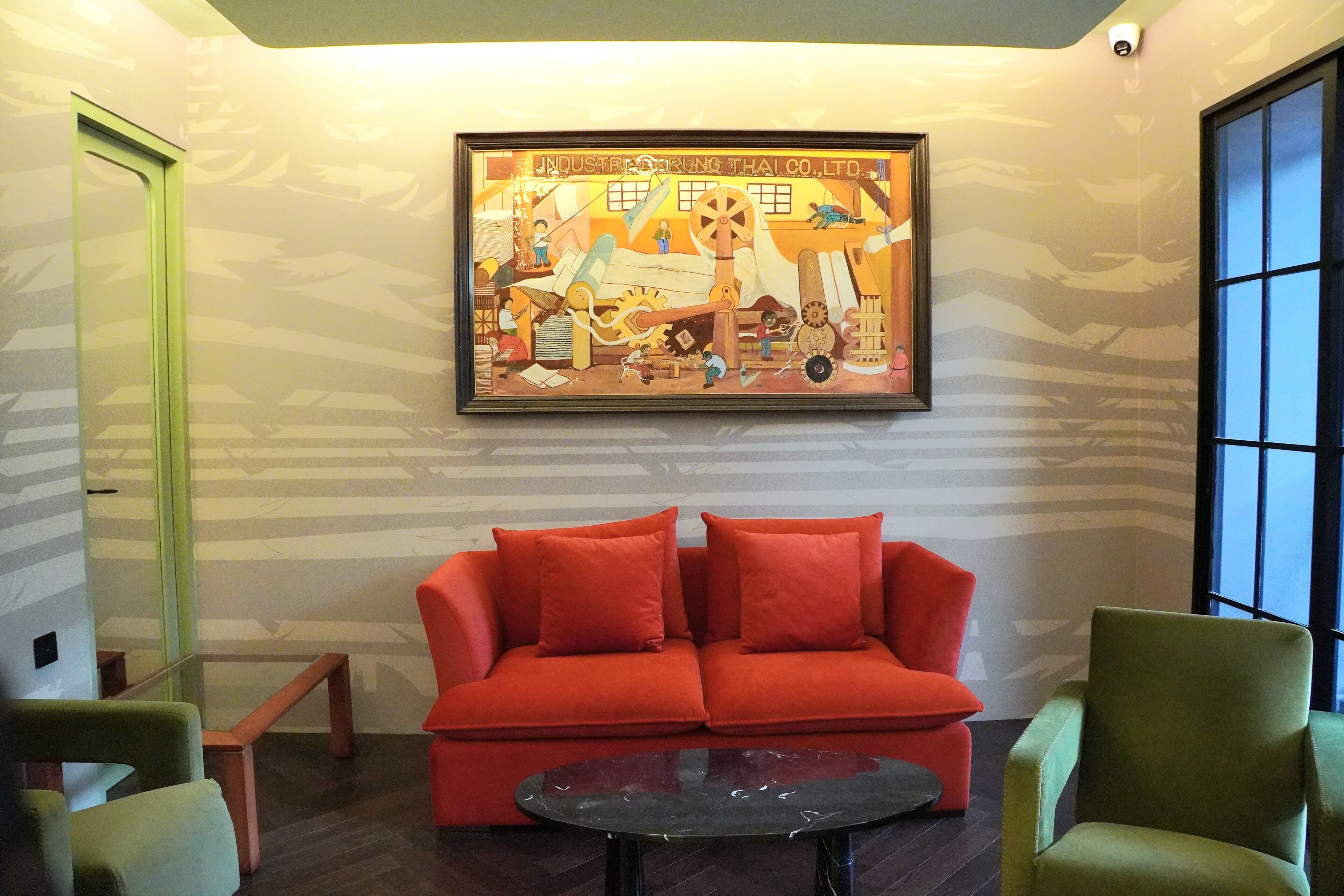 A modern interior with a red sofa, green armchairs, a black coffee table, and a large industrial-themed painting on the wall.
