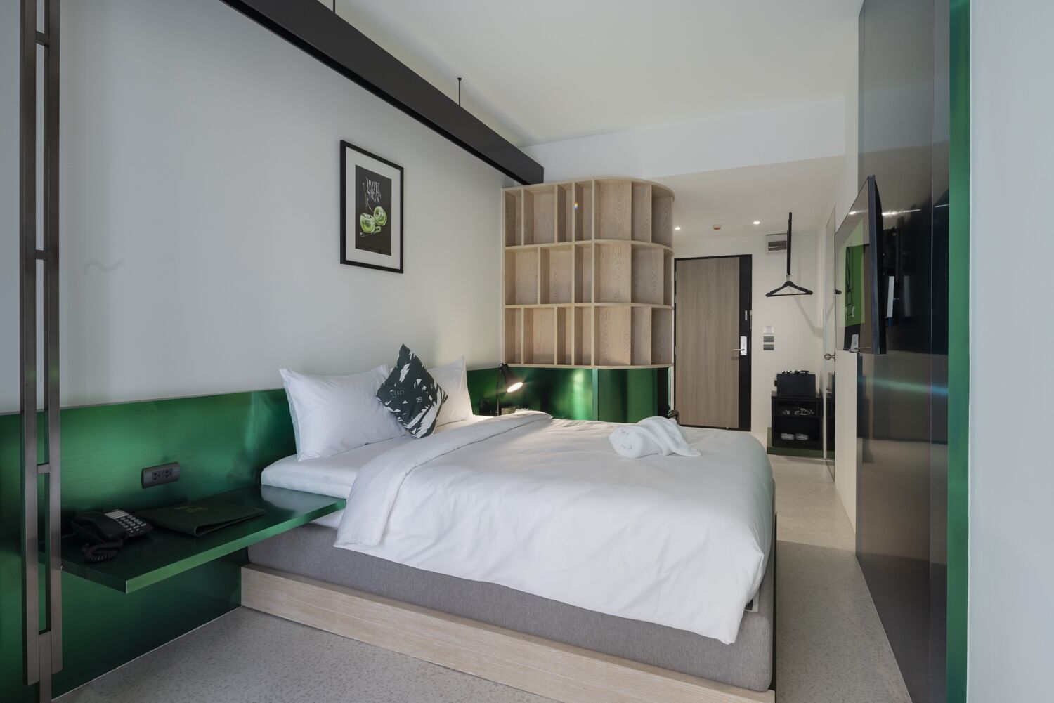 A modern hotel room with a green upholstered headboard, a white bedspread, and a small desk with a telephone.