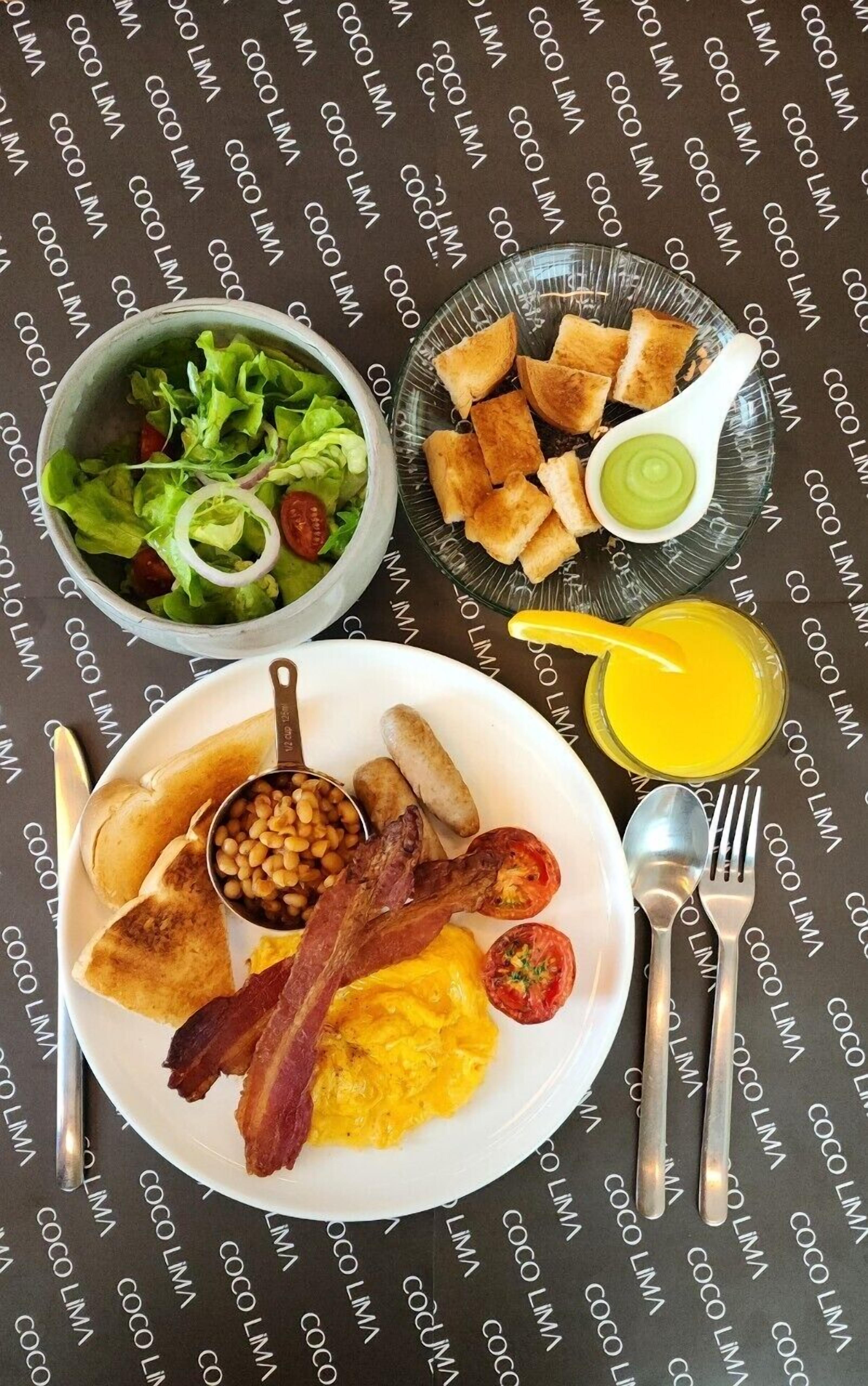 A breakfast plate with eggs, bacon, beans, sausages, toast, and a salad.
