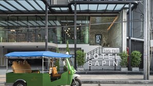 Um tuk-tuk verde e marrom estacionado em frente a um hotel chamado "HOTEL SAPIN".
