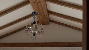 A spacious room with wooden beams, large windows with sheer curtains, a wooden panel wall, and a hanging chandelier. - Betta's Homestay (Jeju City)