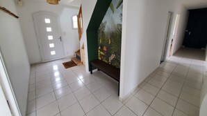 Un pasillo espacioso con piso de baldosas, una escalera con pared de acento verde y una puerta que da a otra habitación.