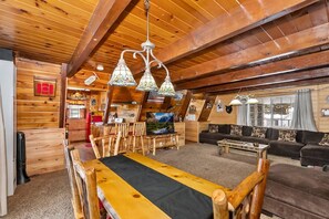 A log cabin interior with a dining area, a sofa, and a television.