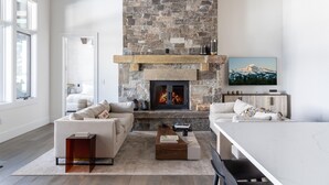 Una sala de estar moderna con chimenea de piedra, dos sofás, una mesa de centro y un televisor sobre un mueble de madera.