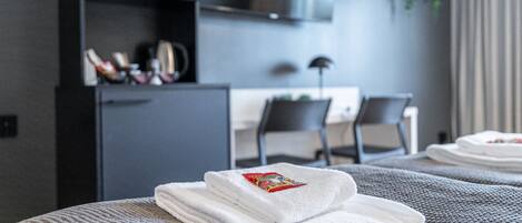 A neatly made bed with folded white towels and a red packet on top.